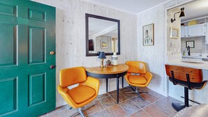 Une pièce avec une porte verte, deux fauteuils orange, une table ronde, un miroir et une coiffeuse en bois avec un lavabo.