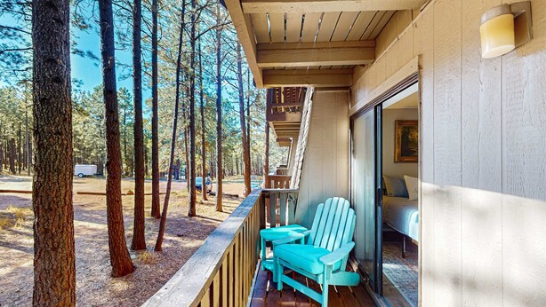 Une terrasse en bois offrant une vue sur une forêt, un lit et une fenêtre avec un luminaire.