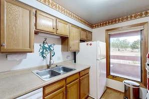 A kitchen with wooden cabinets, a stainless steel sink, a white refrigerator, and a window with a view of the outside. - Cielo Grande - Close to Plaza & Railyard with AC (Santa Fe)
