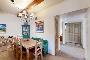 A dining area with a wooden table, chairs, a bench, a chandelier, and wall art. - Cielo Grande - Close to Plaza & Railyard with AC (Santa Fe)