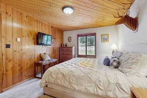 A bedroom with wooden walls, a bed with a quilt, a television, a dresser, and a window with blinds. - Ski Peaks Escape - Walk or Shuttle to Ski Lifts (Angel Fire)
