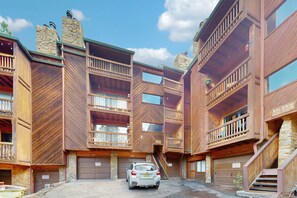 A multi-story wooden building with balconies, a car in the driveway, and garage doors. - Ski Peaks Escape - Walk or Shuttle to Ski Lifts (Angel Fire)