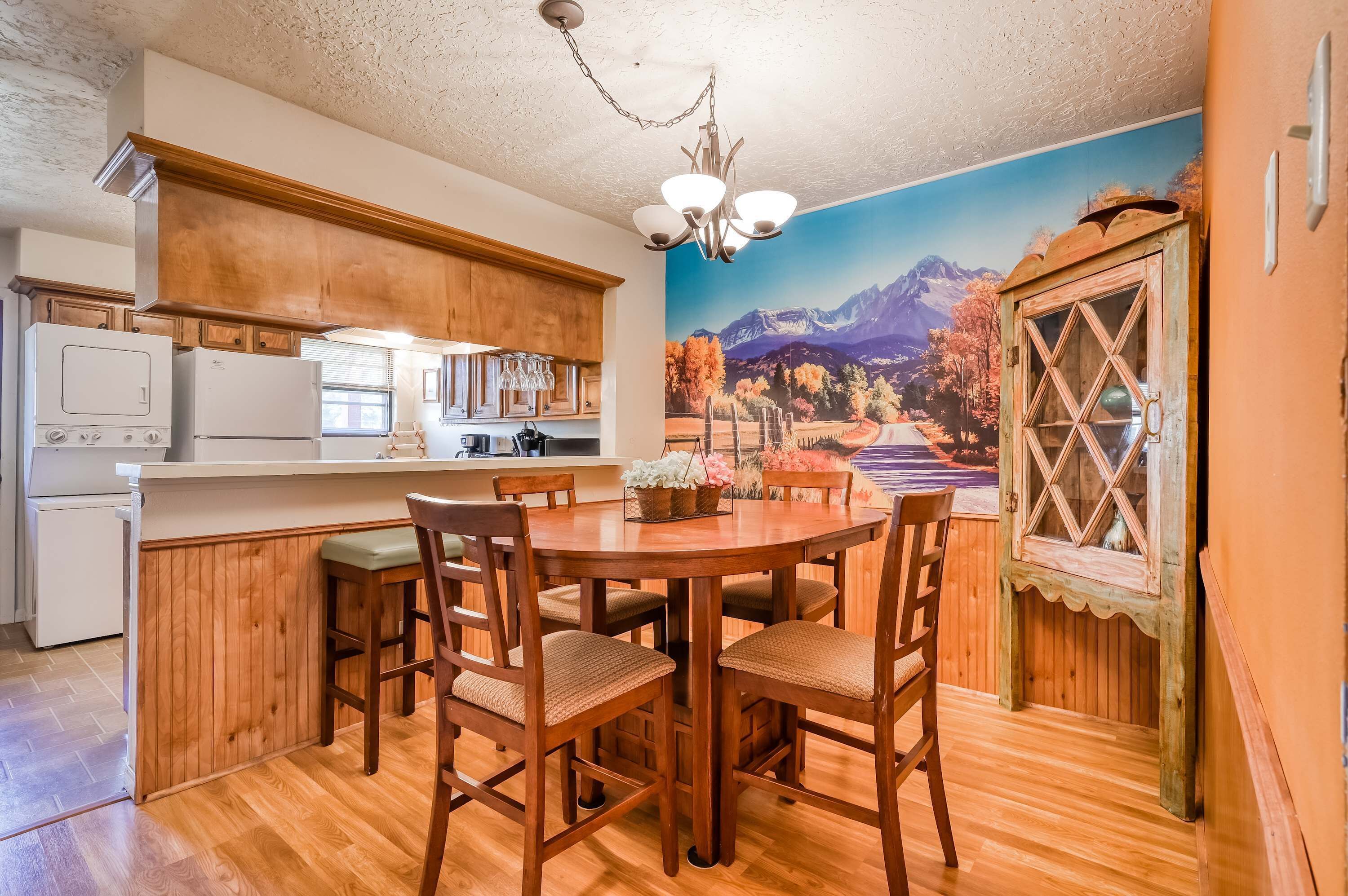 Una cocina con armarios de madera, una mesa de comedor con sillas y un mural de un paisaje montañoso.