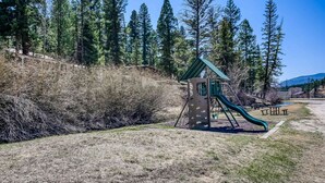A playground with a slide and climbing structure, surrounded by trees and a grassy area. - Creekside Serenade - Hot Tubs & Close to Town (Red River)