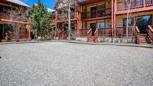 A multi-story building with balconies, a gravel courtyard, and a large evergreen tree. - Creekside Serenade - Hot Tubs & Close to Town (Red River)