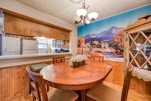 Un comedor con mesa y sillas de madera, una araña y un mural de un paisaje montañoso.
