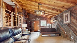 A log cabin interior with a leather couch, wooden shelves, antlers, and a chandelier. - Bigfoot Lodge - Mountain Views & Multiple Decks (Angel Fire)