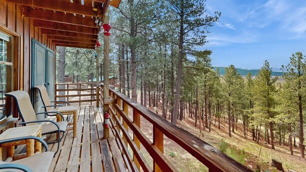 A wooden deck with chairs and a view of a forest. - Bigfoot Lodge - Mountain Views & Multiple Decks (Angel Fire)