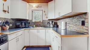 A modern kitchen with white cabinets, a microwave, a stove, and a brick backsplash. - Bigfoot Lodge - Mountain Views & Multiple Decks (Angel Fire)