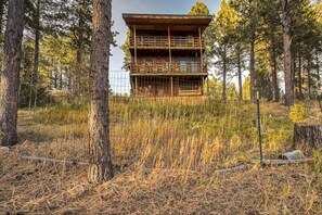 Eine zweistöckige Holzhütte mit Balkon, umgeben von hohen Kiefern und trockenem Gras.