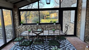 Eine überdachte Terrasse mit einer Steinwand, einem Tisch mit Stühlen und Kübelpflanzen.