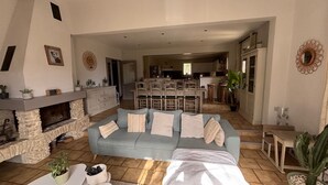 Ein geräumiges Wohnzimmer mit Kamin aus Stein, einem hellblauen Sofa und einer Küche im Hintergrund.
