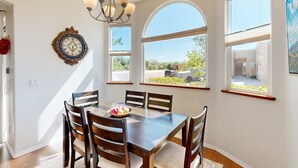 Un comedor con mesa de madera, sillas, una araña y ventanas amplias con vistas.