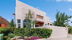 Un edificio moderno con techo plano, grandes ventanales y un jardín cuidado con diversas plantas y flores.