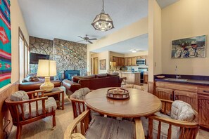 A living room with a round wooden table, a sofa, and a television. - Gold Creek 208 - Walk to Lifts, Slope Views & Deck (Angel Fire)
