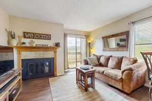 A living room with a fireplace, a sofa, a coffee table, a TV, and a 'welcome' sign. - Christi Villa 100 - Near Ski, Hike, Bike & Dining (Angel Fire)