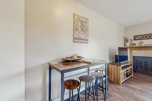 A kitchen area with a wooden table, bar stools, a television, and a fireplace. - Christi Villa 100 - Near Ski, Hike, Bike & Dining (Angel Fire)