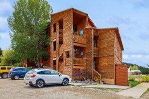 A multi-story wooden building with balconies, a staircase, and a parking area with cars. - Christi Villa 100 - Near Ski, Hike, Bike & Dining (Angel Fire)