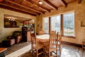 A rustic interior with a wooden dining table, chairs, a leather sofa, and a large window. - Casa Grande - 5 King Suites, Hot Tub, Arcade (Angel Fire)