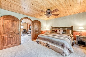 A bedroom with a wooden ceiling, a bed with a striped blanket, two wooden doors, and a ceiling fan. - Casa Grande - 5 King Suites, Hot Tub, Arcade (Angel Fire)