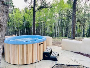 A hot tub with wooden panels, a set of steps, and a concrete patio in a forested area. - Casa Grande - 5 King Suites, Hot Tub, Arcade (Angel Fire)