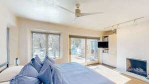 Quarto com cama, ventoinha no teto, lareira e uma janela grande.