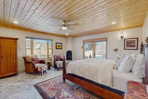 A bedroom with a wooden ceiling, a bed with white bedding, a chair, a rug, and a wooden wardrobe.