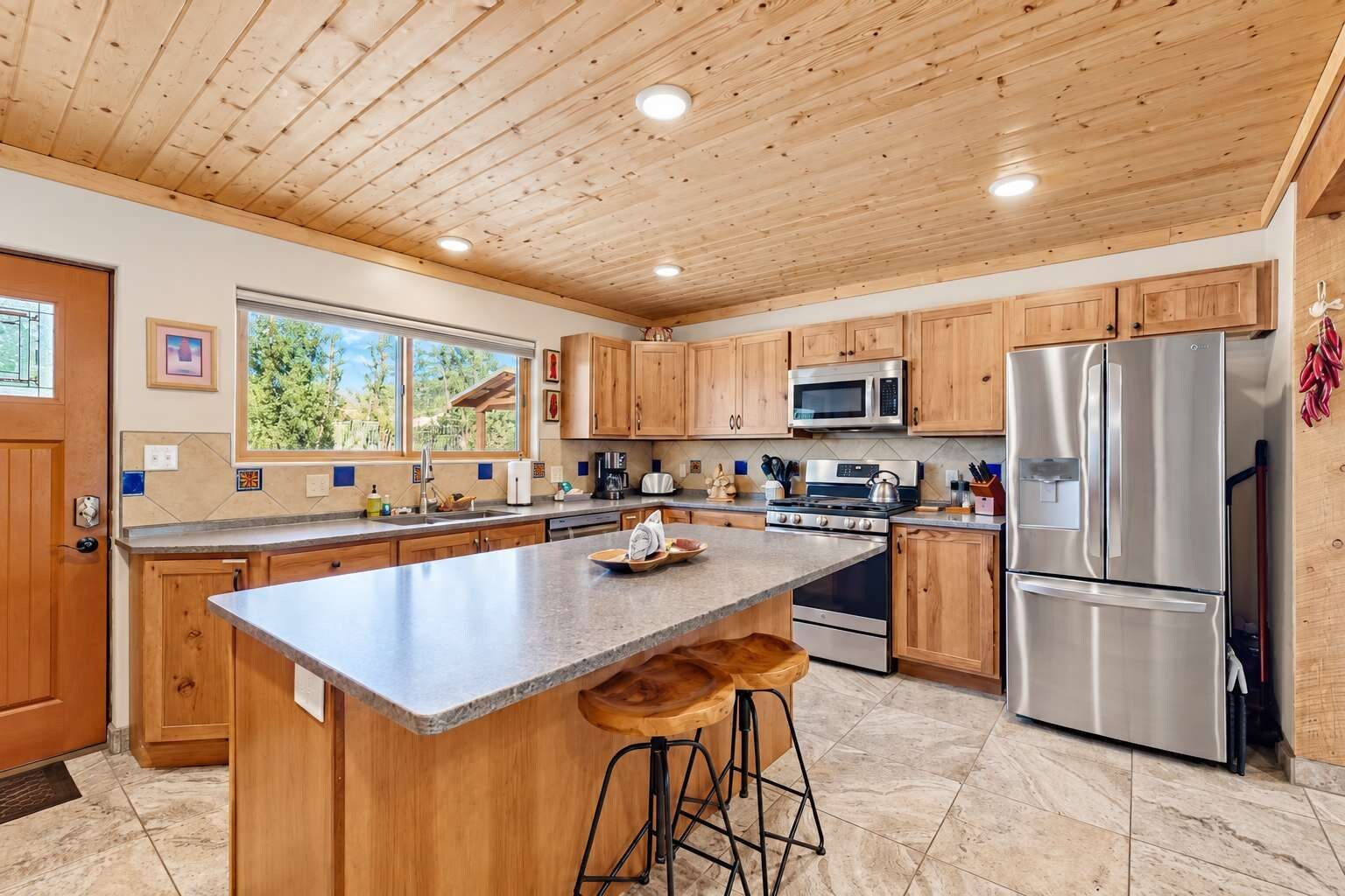 A modern kitchen with wooden cabinets, stainless steel appliances, and a large island with bar stools.