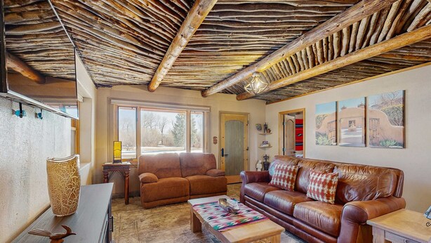 A living room with a rustic ceiling, leather sofas, a wooden coffee table, and a large window. - Casa de Rufina - Mountain Views, Firepit & Pets (Arroyo Seco)
