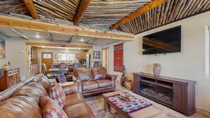 A living room with leather sofas, a wooden coffee table, a TV, and a fireplace. - Casa de Rufina - Mountain Views, Firepit & Pets (Arroyo Seco)