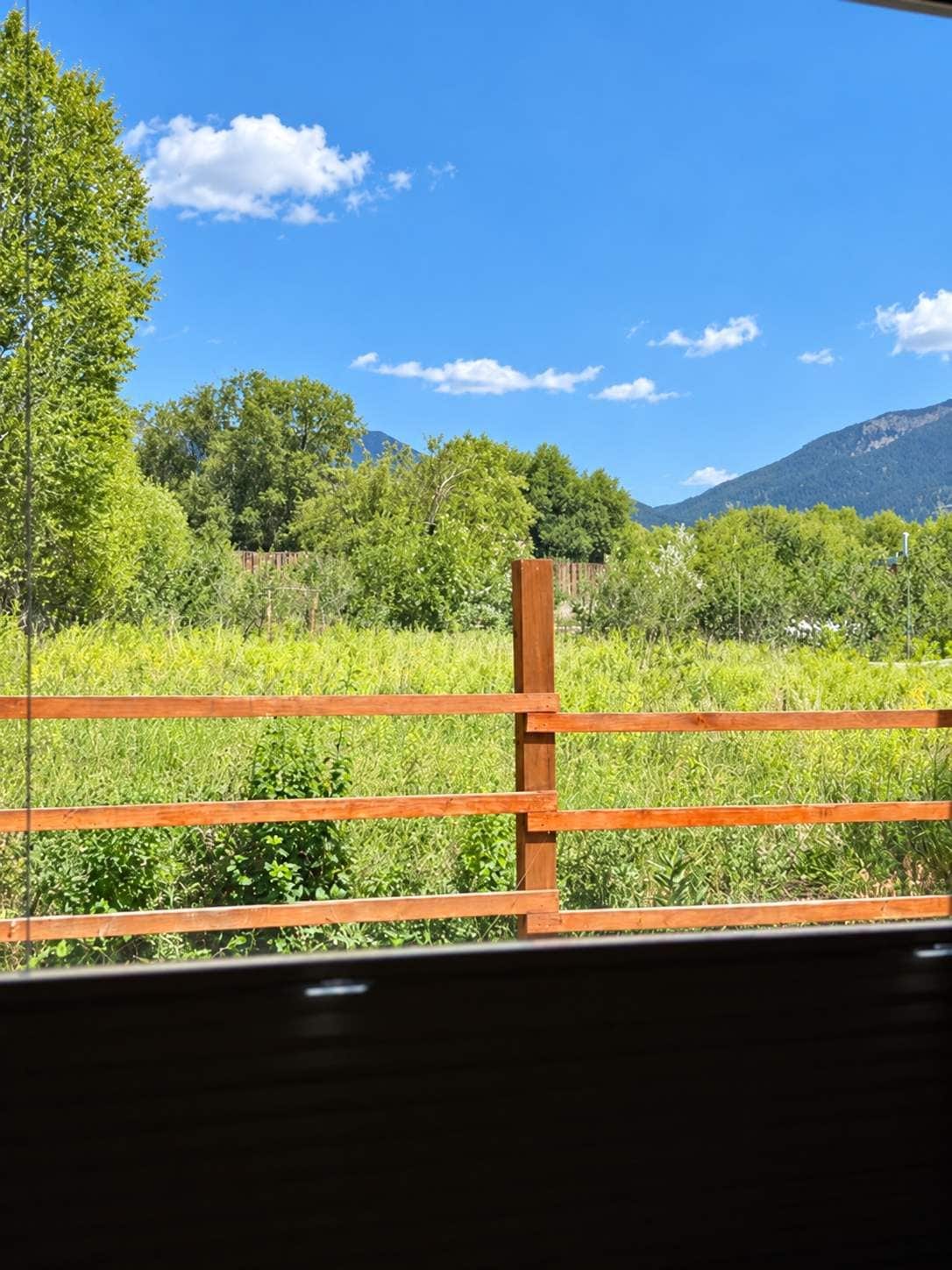 A wooden fence with a view of a green field and trees in the background.