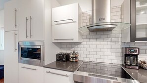 A modern kitchen with stainless steel appliances, white cabinetry, and a glass backsplash. - Kachina Ridge Dreams - Walk to Lifts & Huge Views (Taos Ski Valley)
