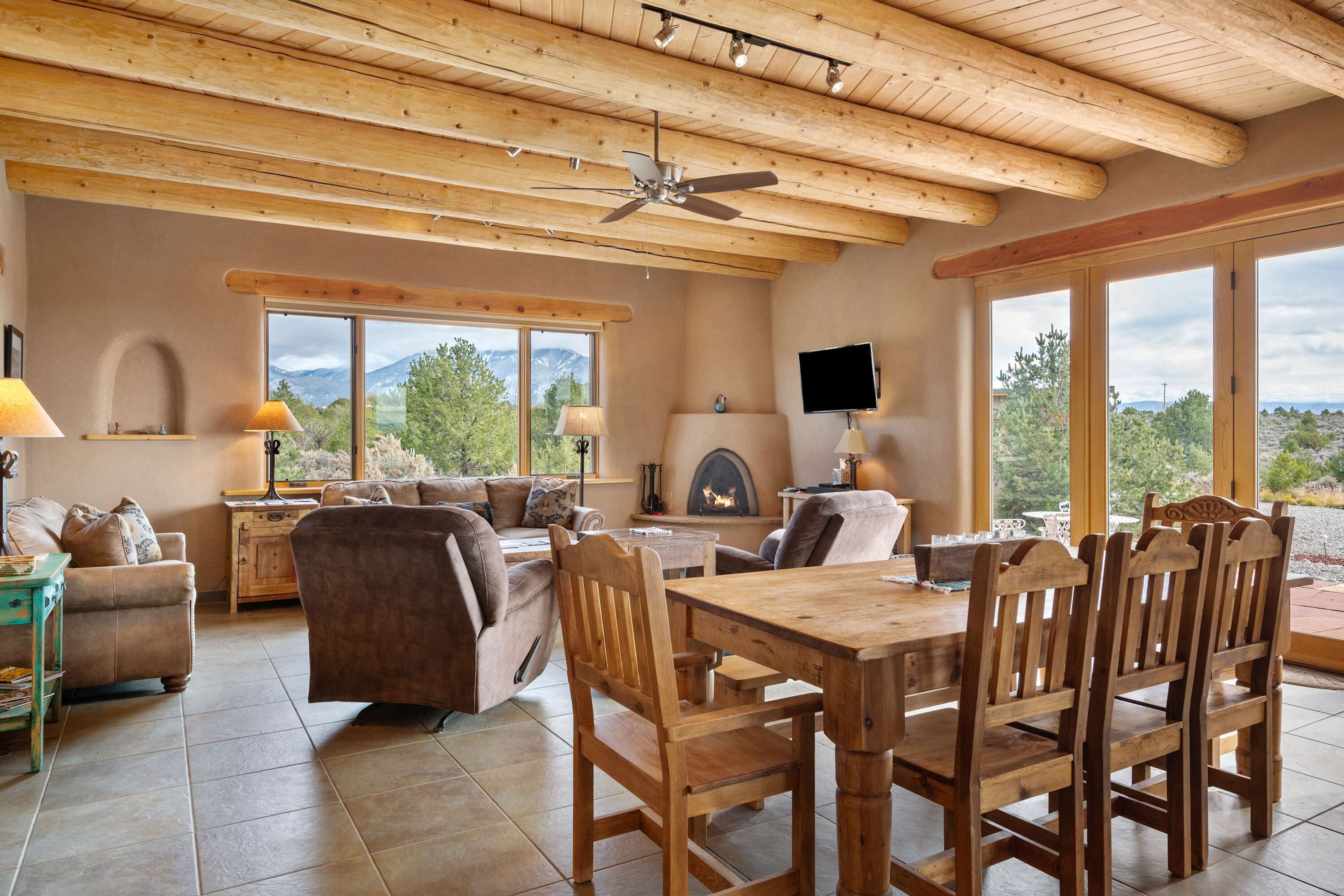 A spacious living area with a wooden ceiling, a fireplace, and large windows offering a mountain view.