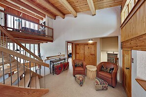 A spacious loft with a wooden staircase, a cozy seating area with a leather armchair and ottoman, and a wooden door. - Predock 3C - Walk to Lifts, Hiking, Dining & Shops (Taos Ski Valley)