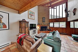 Ein geräumiges Wohnzimmer mit Kamin, Holzbalkendecke und großen Fenstern.