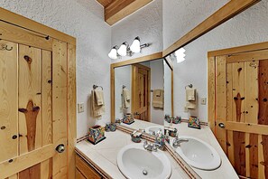 Ein Badezimmer mit Holzwandverkleidung, zwei Waschbecken, einem Spiegel und einer Leuchte darüber.
