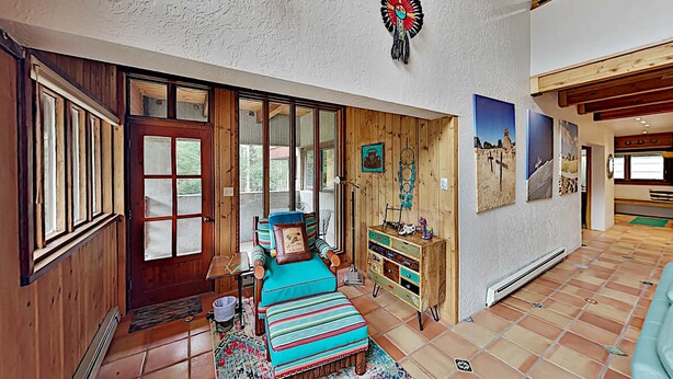Ein Zimmer mit Holztür, einer Bank mit gestreiften Kissen, einem Holzkasten und einer Wand mit gerahmten Bildern.