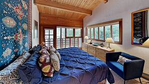 Ein Zimmer mit einem Bett, einem blauen Sofa, einer Holzbalkendecke und großen Fenstern.
