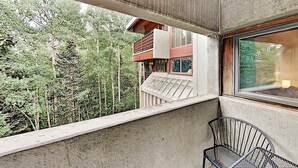Ein Balkon mit Blick auf einen Wald, ein Fenster und ein Metallstuhl.