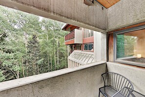A balcony with a view of a forest, a window, and a metal chair. - Predock 3C - Walk to Lifts, Hiking, Dining & Shops (Taos Ski Valley)