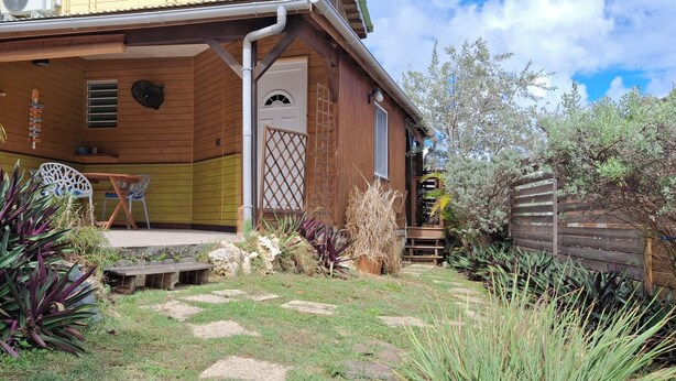 A wooden house with a porch, outdoor seating, and a garden with various plants. - Havre de Paix next to the coast, 5 minutes from Petit-havre beach (Le Gosier)