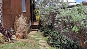 A wooden house with a stone pathway leading to a wooden deck, surrounded by various plants and a clear sky. - Havre de Paix next to the coast, 5 minutes from Petit-havre beach (Le Gosier)