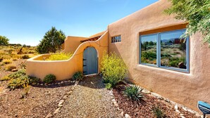 Une maison aux murs recouverts d’enduit, dotée d’une entrée en arc de cercle, d’une grande fenêtre et d’un jardin aménagé.