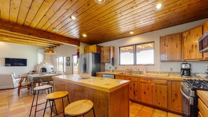 Une cuisine avec des meubles de rangement en bois, un îlot central doté de tabourets, un réfrigérateur et une cuisinière.