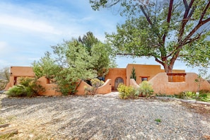 A building with a stucco exterior, a large tree in front, and a gravel driveway.