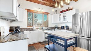 A modern kitchen with a large island, stainless steel appliances, and a view of the outdoors through a window.
