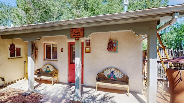 Un edificio con una puerta roja, dos bancos y un cartel que dice 'Casita Antonio'.