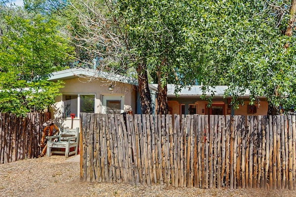 A rustic wooden fence, a house with a garage, and a tree in front.