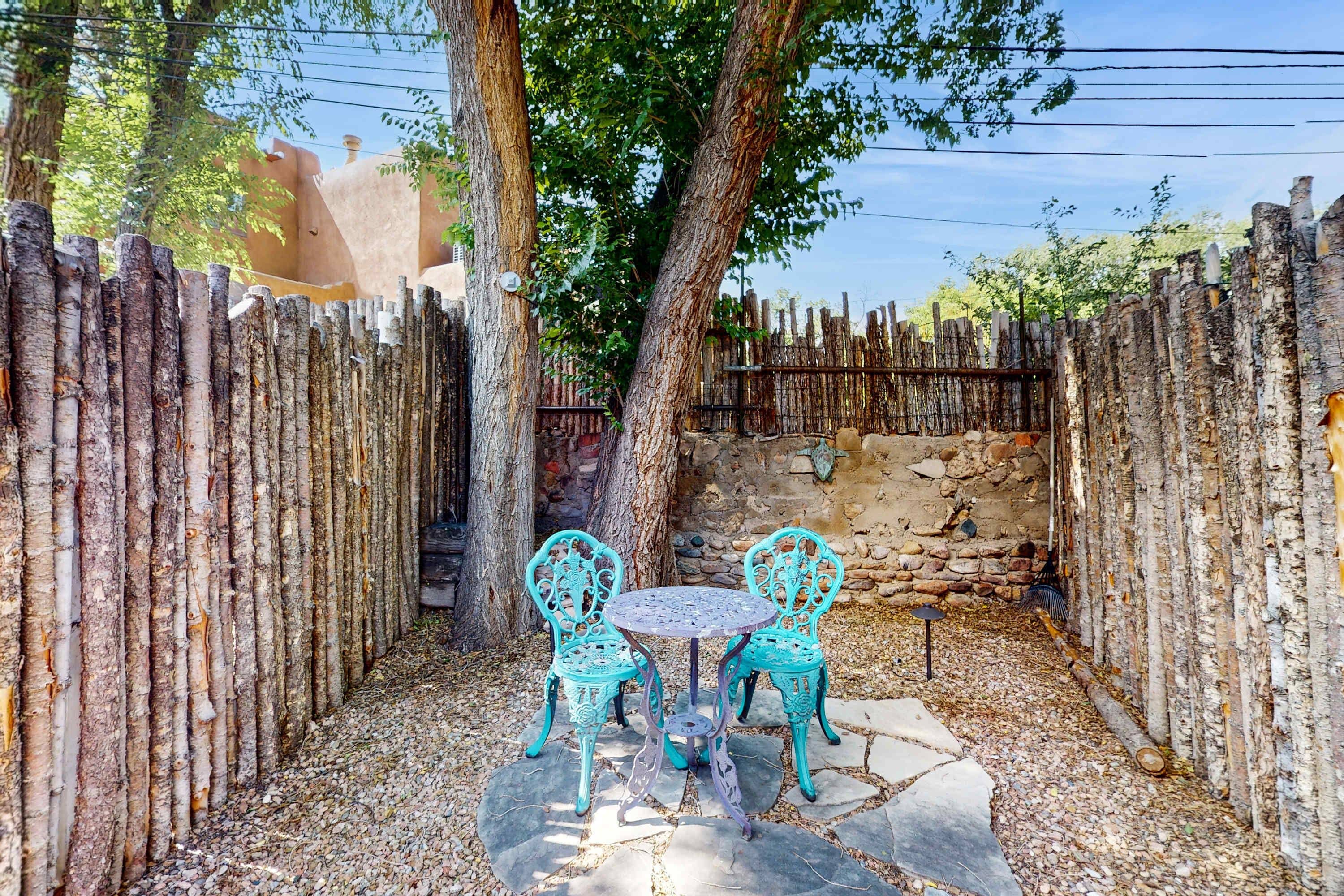 A rustic outdoor seating area with a stone table and chairs, surrounded by a wooden fence and trees.