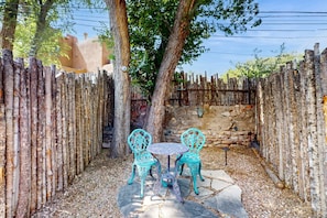 A rustic outdoor seating area with a stone table and chairs, surrounded by a wooden fence and trees.